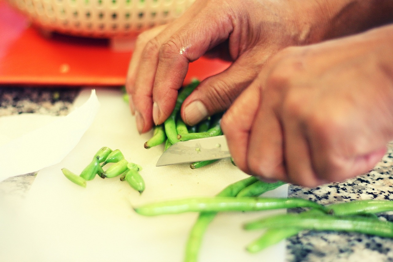 Mains qui coupent des haricots verts sur une planche à découper