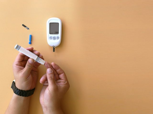 Mains tenant un lecteur de glycemie et une lancette sur fond orange
