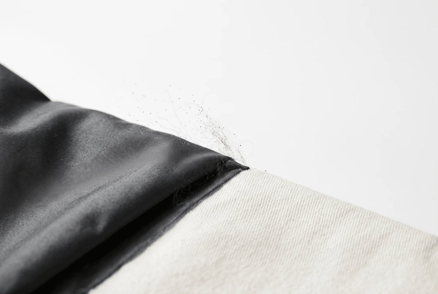 Gros plan de fibres noires effilochées s'échappant d'un tissu synthétique sombre contre du coton clair